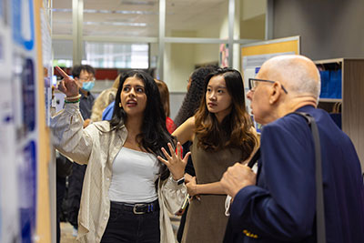 Sana Ansari presents AI research, pointing to a wall of visuals while two individuals listen