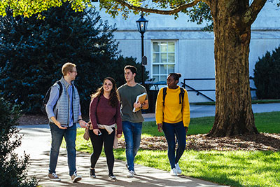 Four Emory students walking and talking among sunlit trees