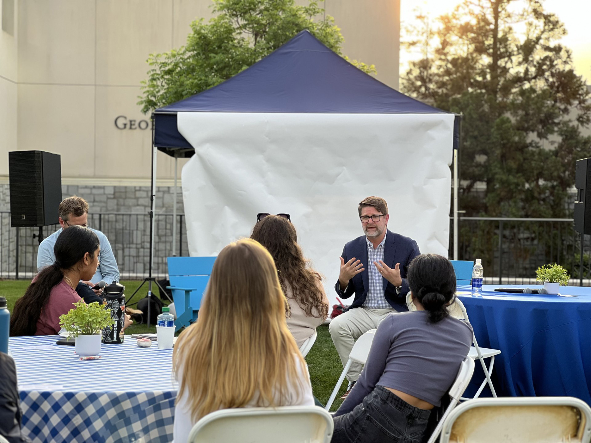 people at an outdoor dinner listen intently to a seated speaker